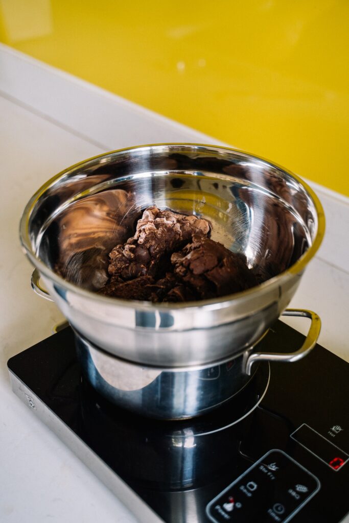 A stainless bowl with meat on top of a silver stainless steel cooking pot on a black electric stove