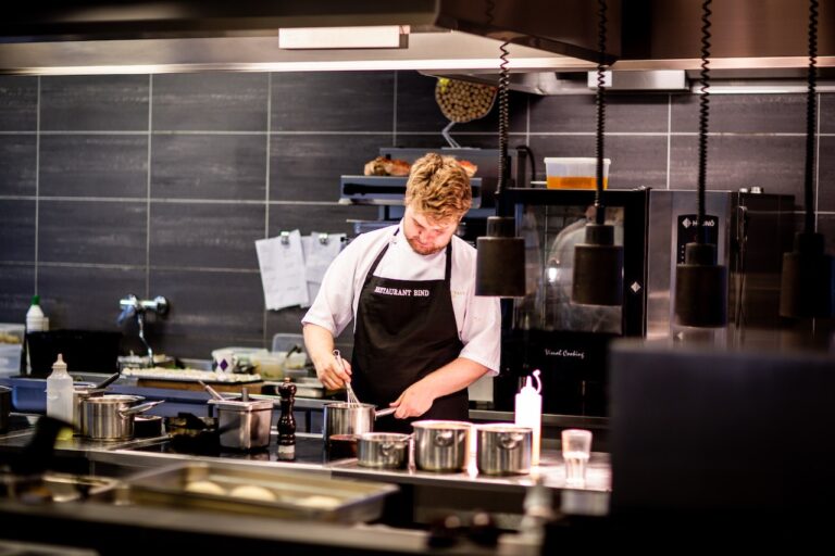 A man in a white short sleeve chef uniform and a black apron cooking on silver stainless steel in the kitchen