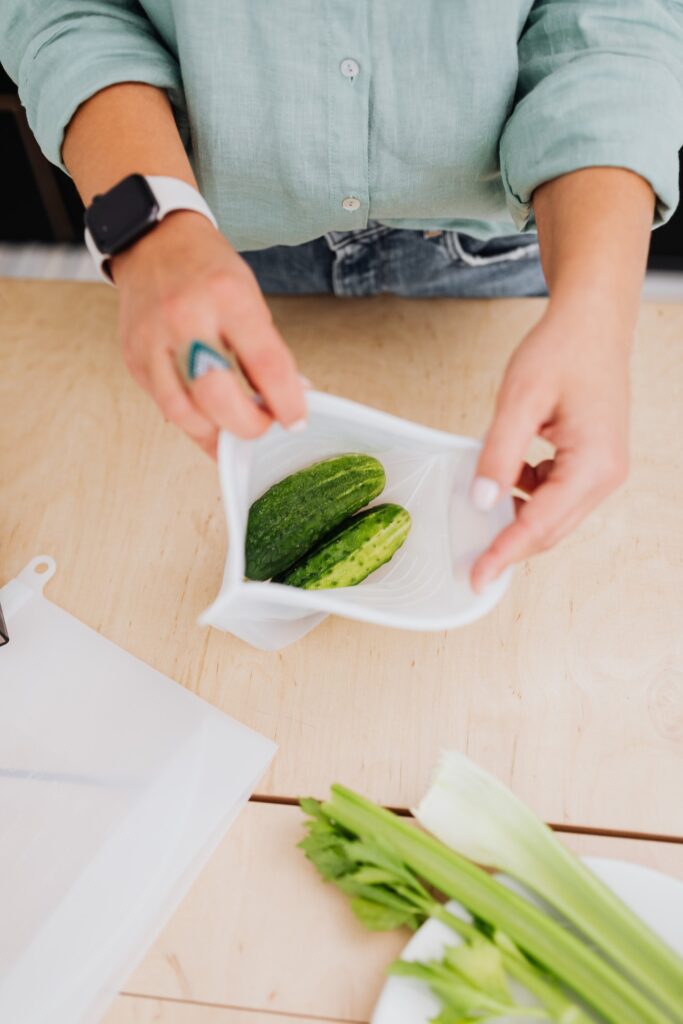 A person in green long sleeves and blue pants packing cucumbers on a zip lock bag on a wooden table