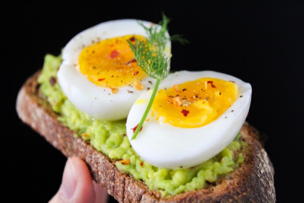 A sliced egg with herbs on top of green salad with brown bread held by a person