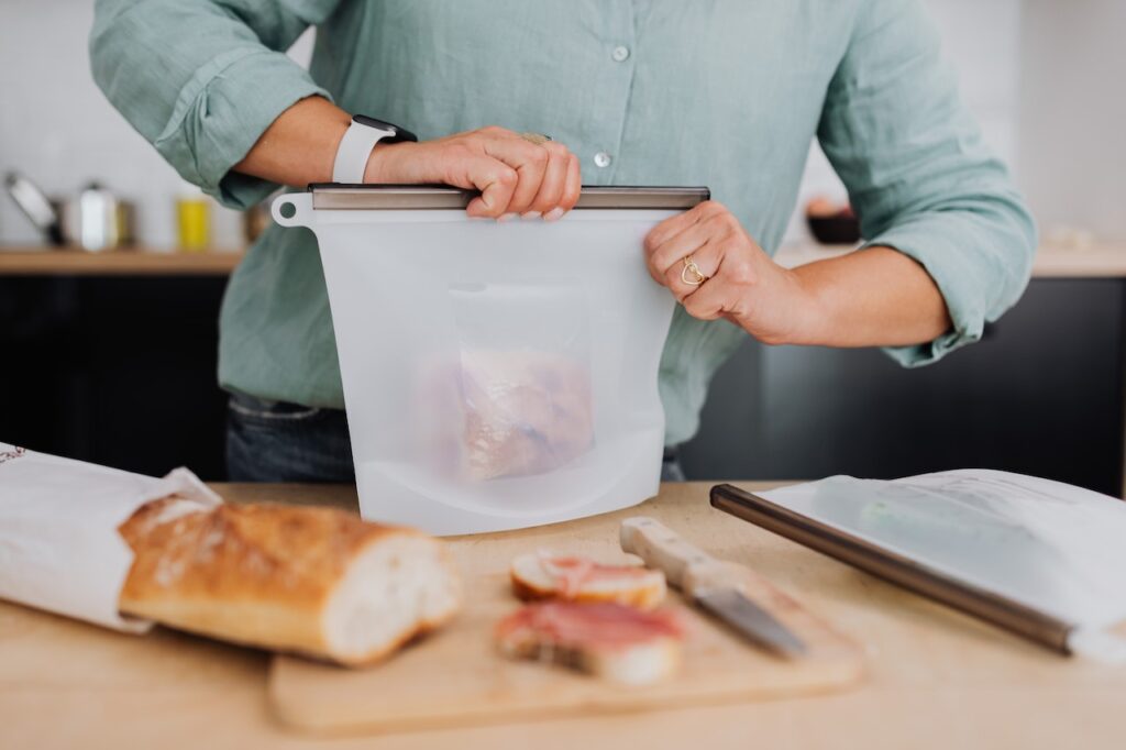 A person in green long sleeves is closing a white plastic container with bread inside