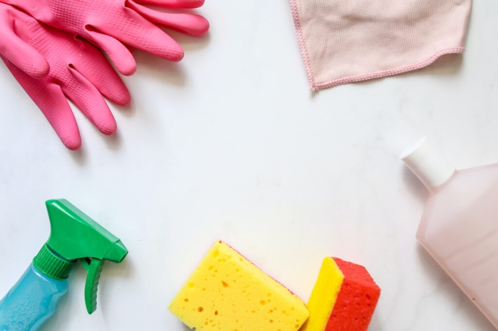 Detergent was placed on a spray bottle on top of pink gloves beside sponges and a pink towel