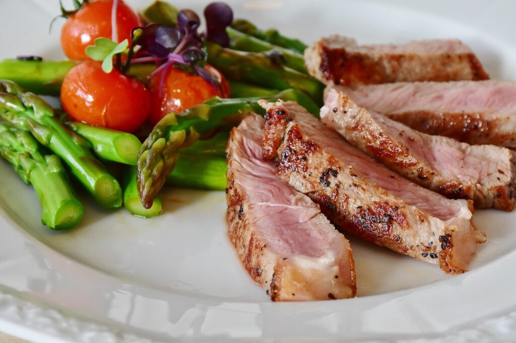 A slice of cooked meat with green asparagus and red cherry tomatoes on a white plate