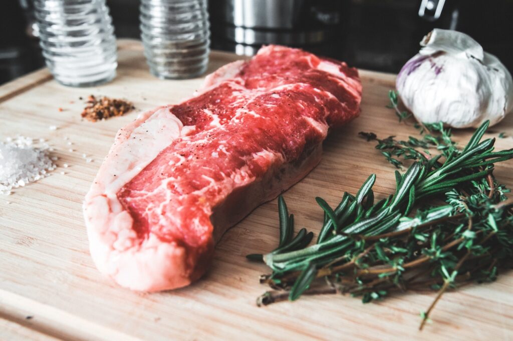 Raw red meat beside different spices placed on a brown wooden chopping board