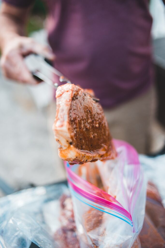 A person placing marinated pork using a thong on a silicone bag