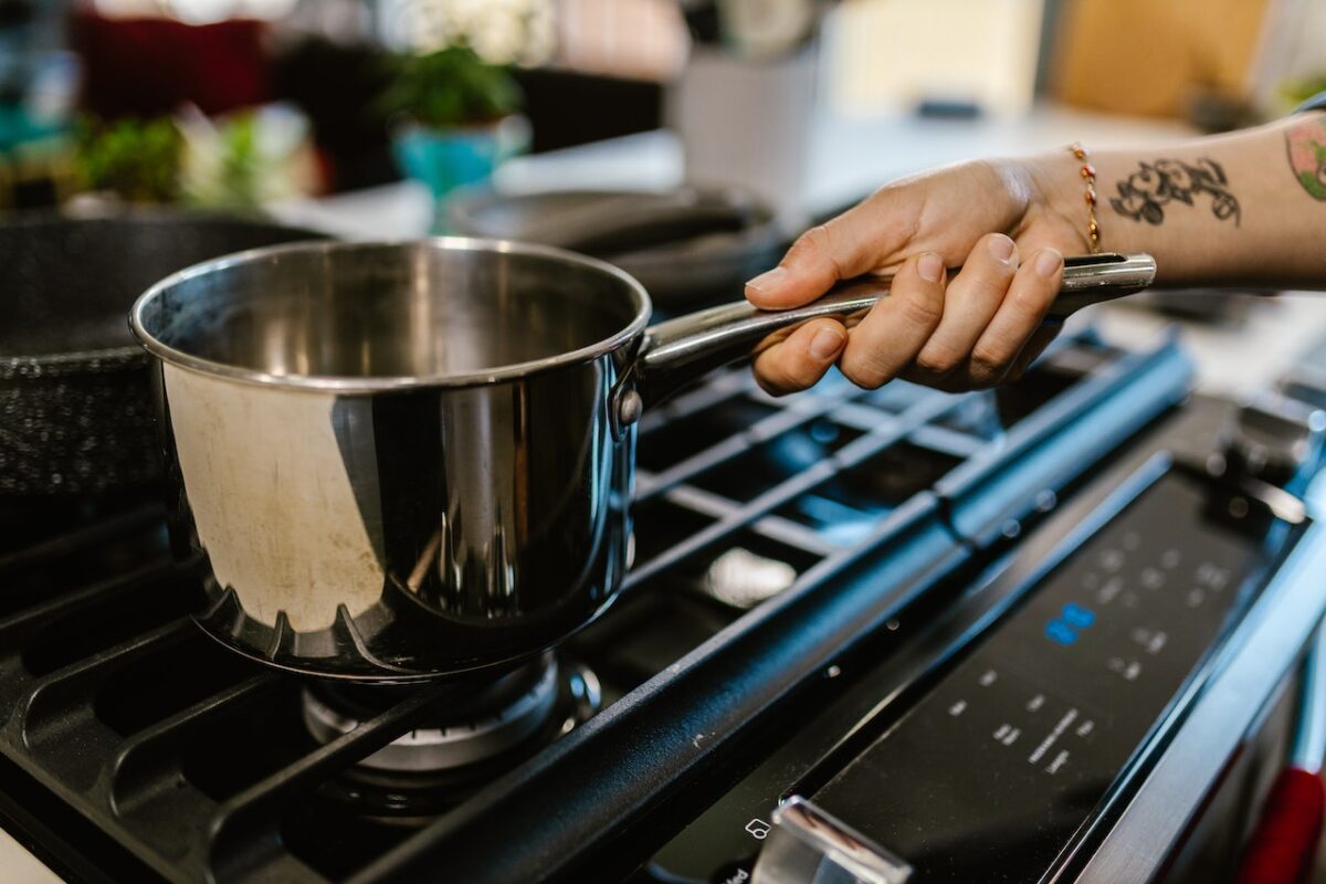 A person holding a stainless steel pot near a ceramic pot on top of a black stove