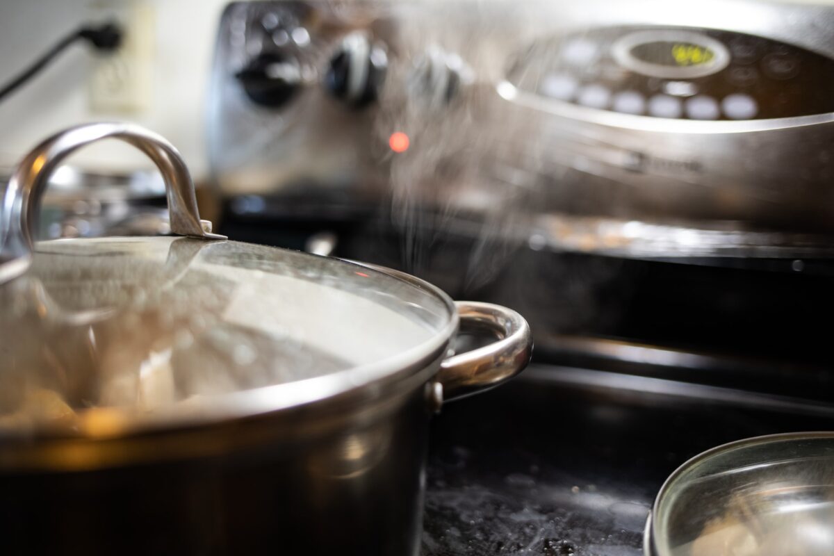 A stainless steel cooking pot with stainless steel lid on top of a black gas range