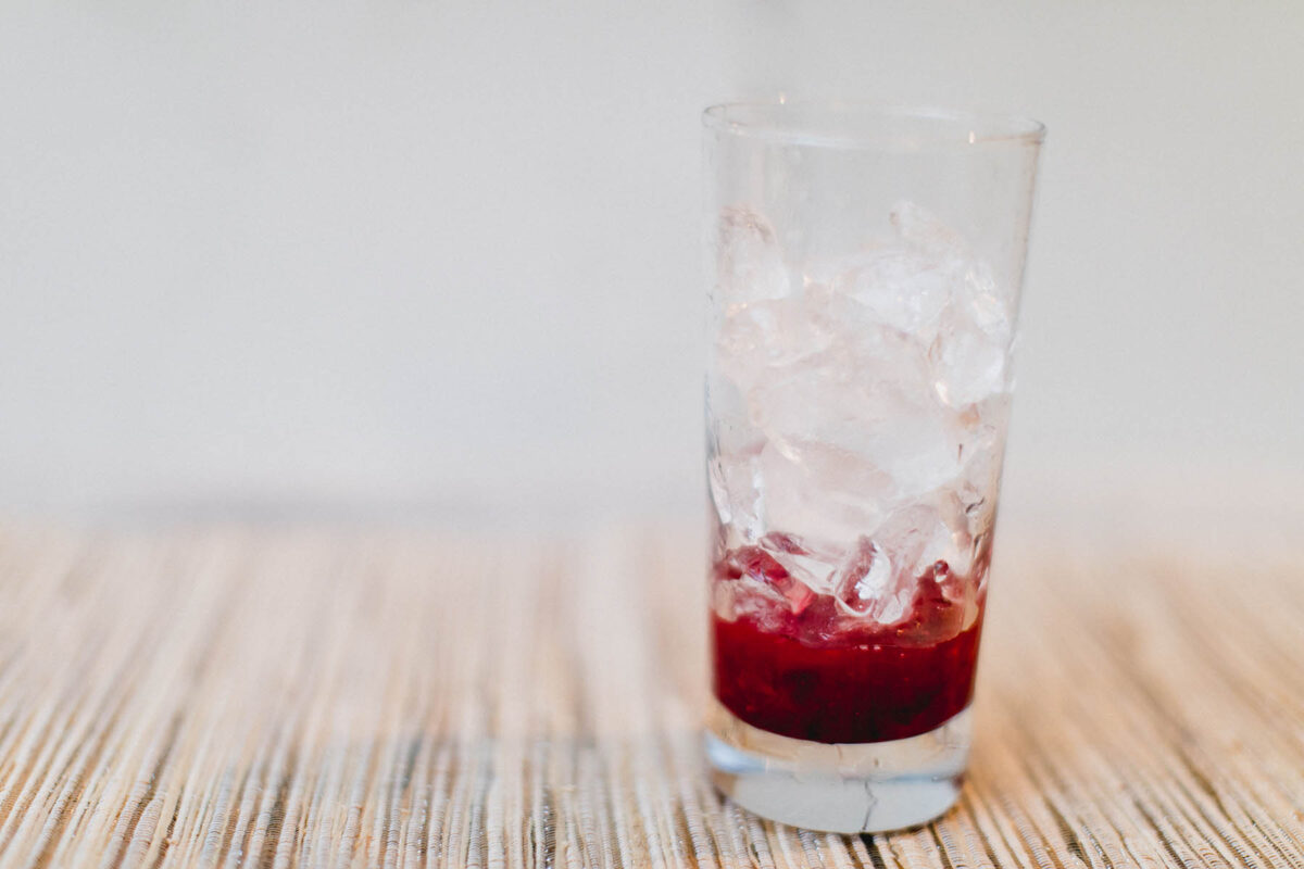 Cranberry sauce and ice in a glass that's going to be used for a cranberry tequila sunrise cocktail