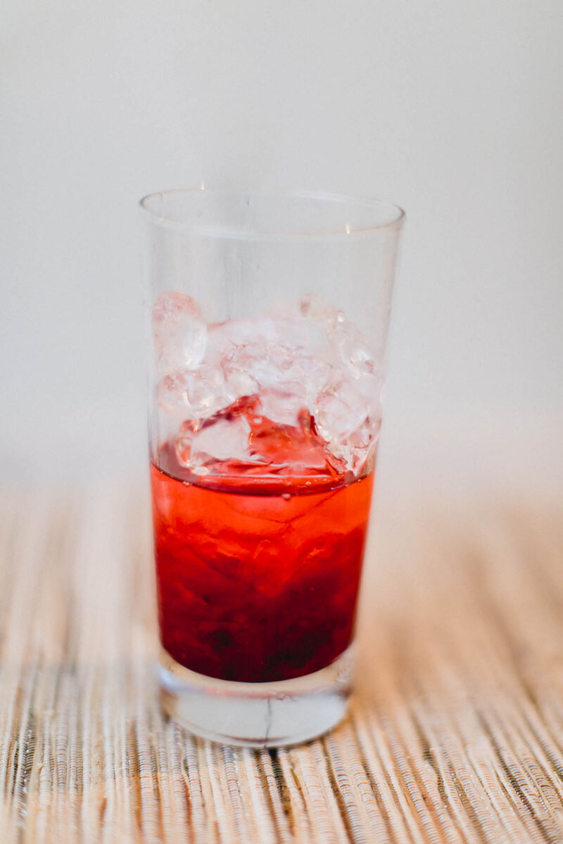 Cranberry sauce, ice, and grenadine in a glass that's going to be used to make a tequila sunrise cocktail