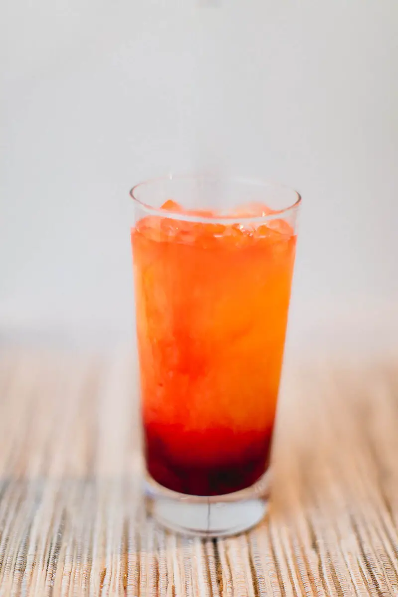 Cranberry tequila sunrise cocktail in a tall glass placed on a light brown placemat in the dining room