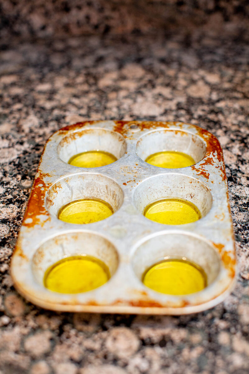 Olive oil poured into a silver muffin tin sitting on a brown granite countertop