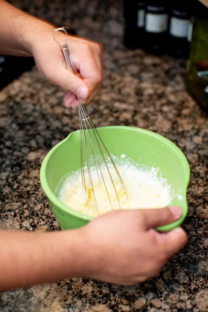 Man mixing together ingredients for Yorkshire popovers in a green mixing bowl using a whisk