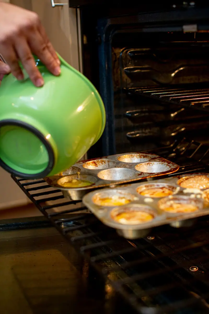 Man pouring Yorkshire popover batter into a muffin tin that's inside the oven