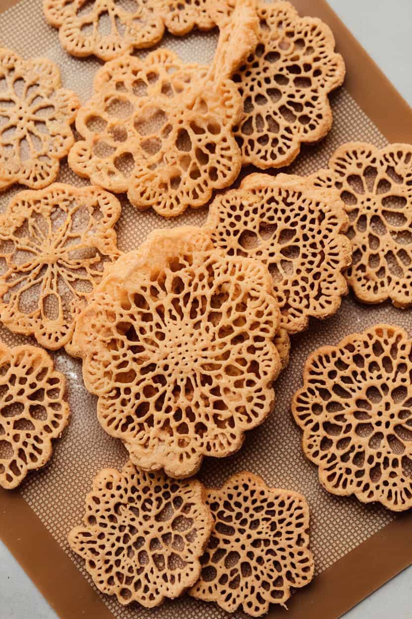 Photo prompt: Indoors, delicate lace cookies cooling flat on a silicone mat, golden and see-through, no text or logos.