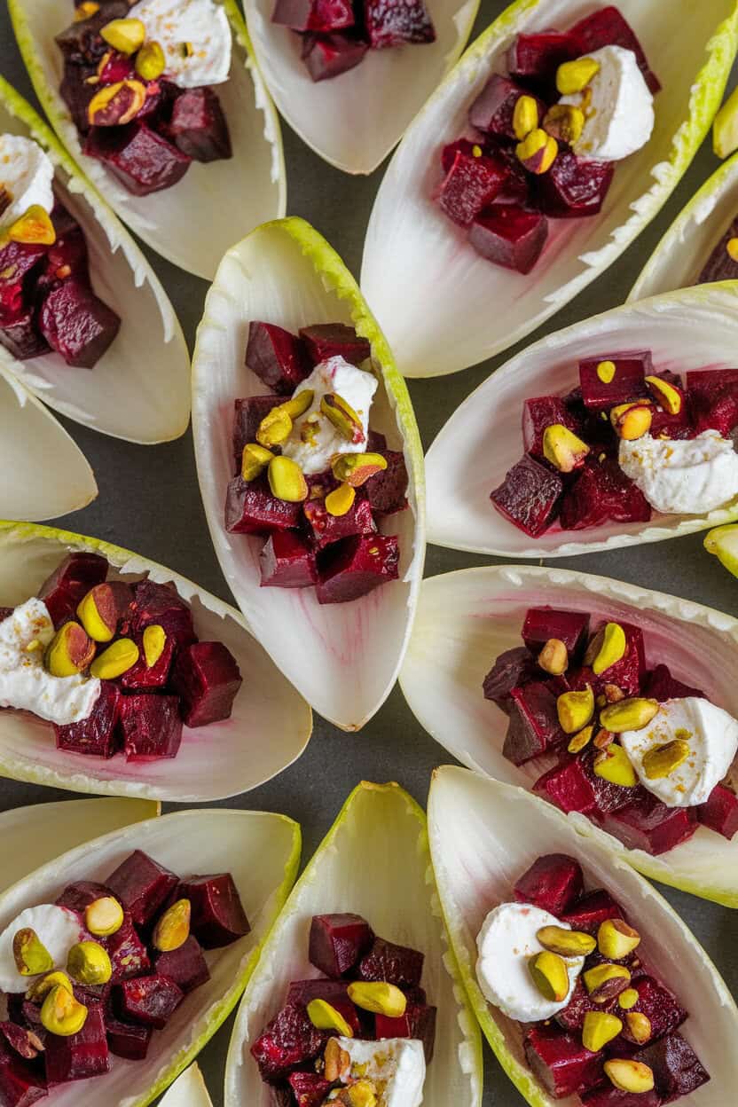 Photo of endive leaves indoors filled with diced roasted beets and dollops of goat cheese, sprinkled with chopped pistachios; overhead angle, no logos