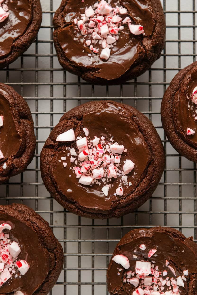 Indoor close-up of rich, glossy brownie cookies topped with crushed peppermint candy on a cooling rack; no branding.