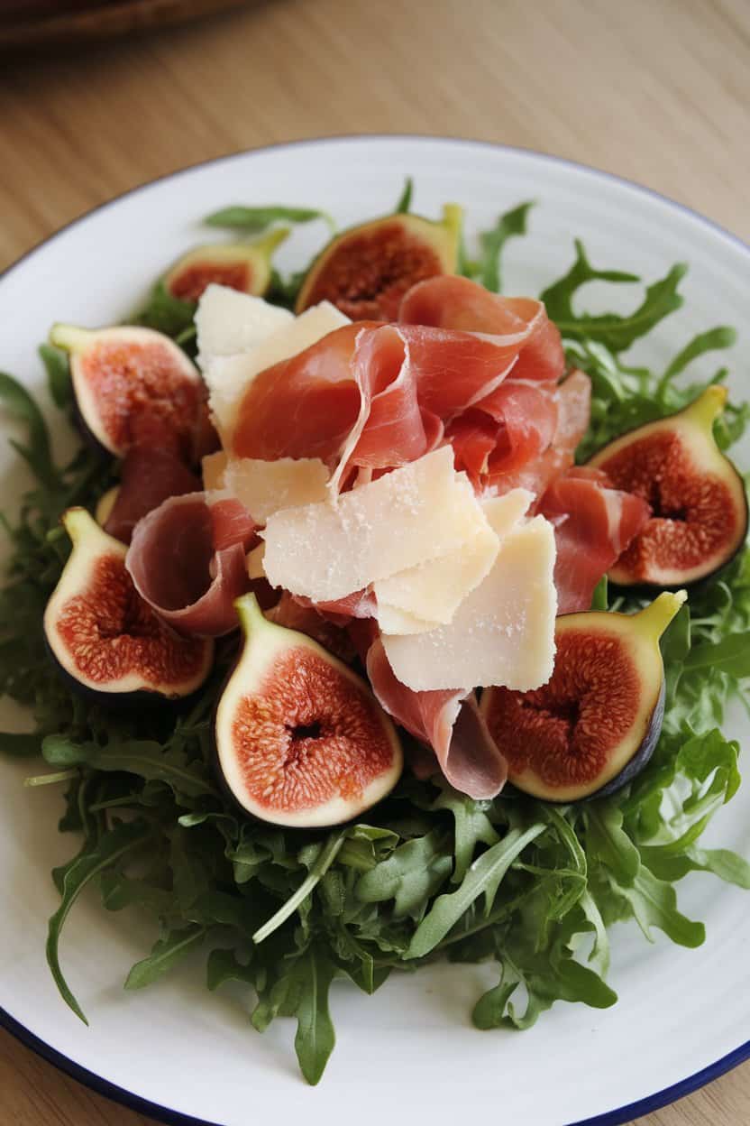 Indoor photo of peppery arugula leaves topped with sliced fresh figs, thin ribbons of prosciutto, and shaved Parmesan, lightly dressed. No text or logos.
