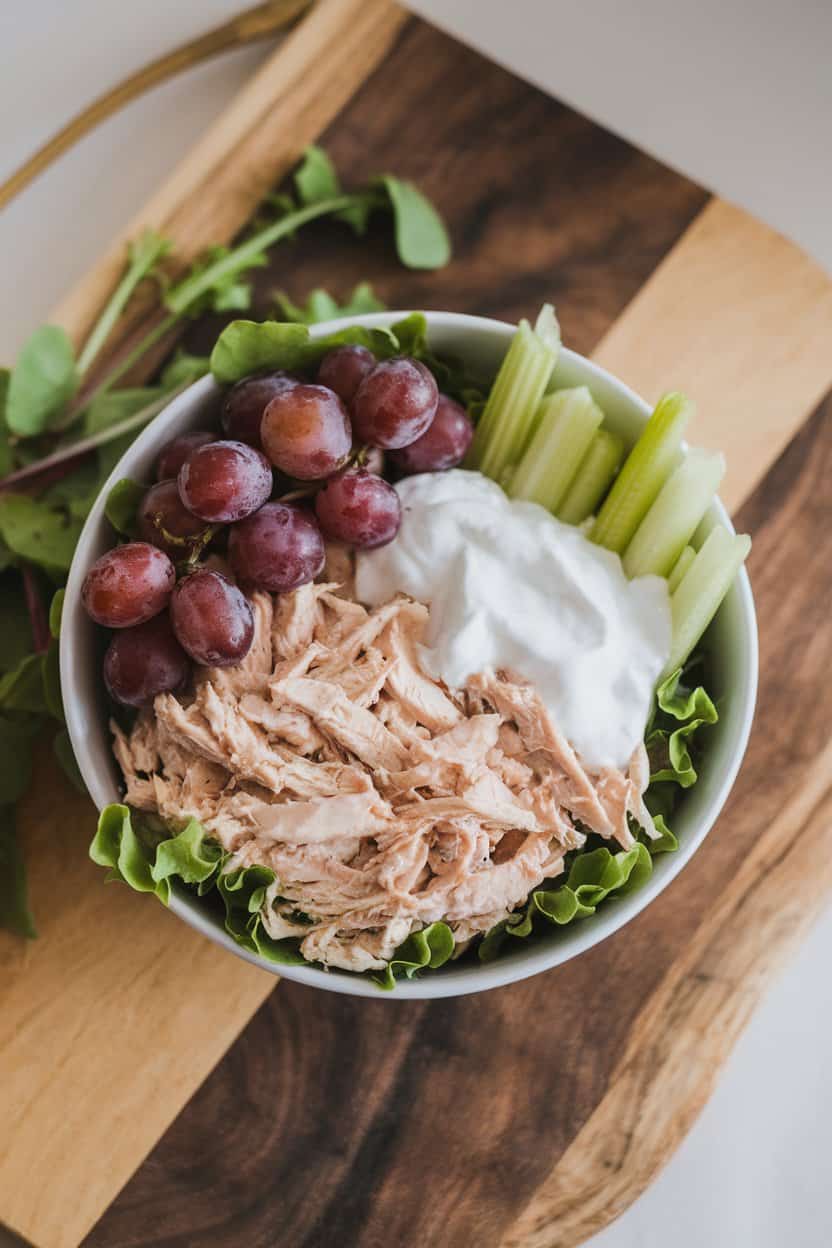 Indoor photo of a bowl of chicken salad made with shredded chicken, Greek yogurt, grapes, and celery; served on leafy greens, no text or logos